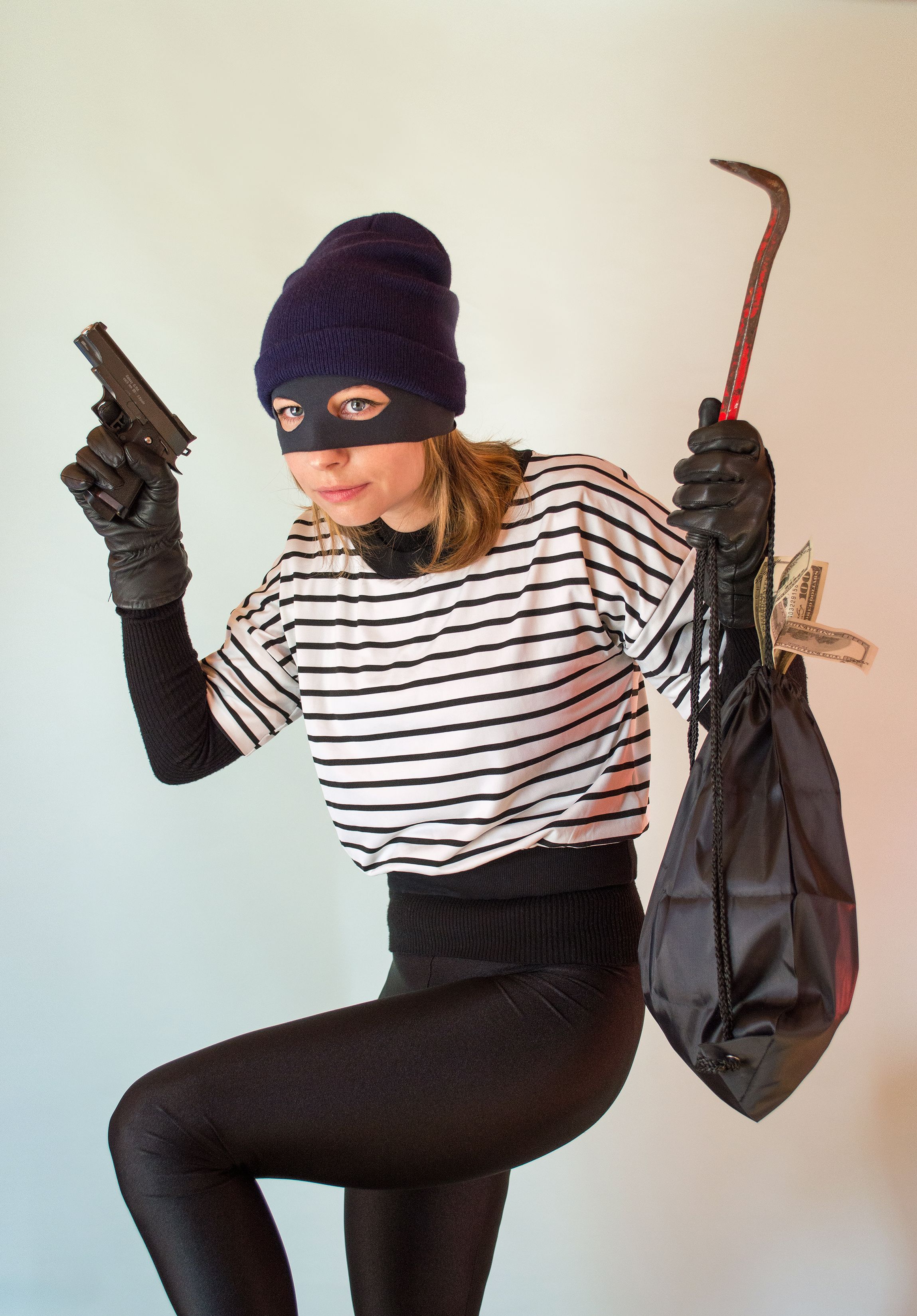 A picture of a woman in a robber costume with a bag and a toy gun